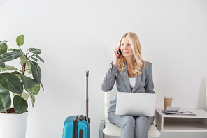 happy mature businesswoman working with laptop and talking by phone while waiting for trip
