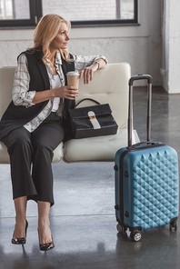 beautiful middle aged woman with suitcase and coffee waiting for flight