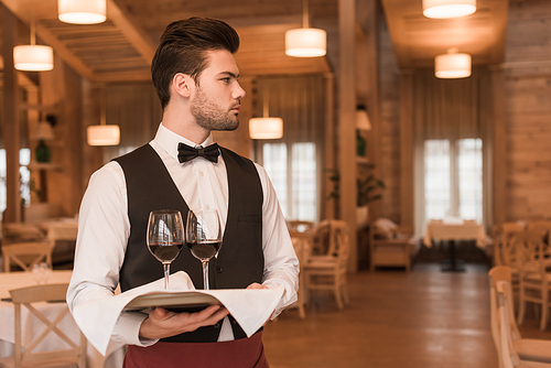 waiter holding tray with glasses with red wine and looking away