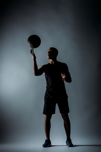 african american sportsman spinning basketball ball on finger in dark room