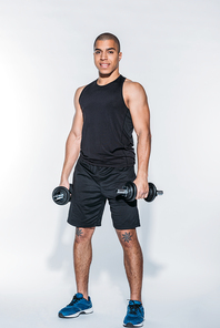 smiling african american sportsman standing with dumbbells