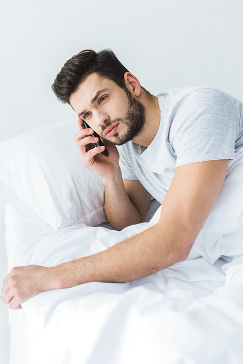 bearded man lying on bed and talking on smartphone