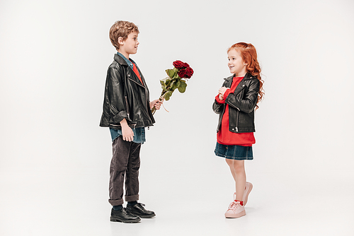 boy presenting roses bouquet to his beautiful little girlfriend isolated on grey