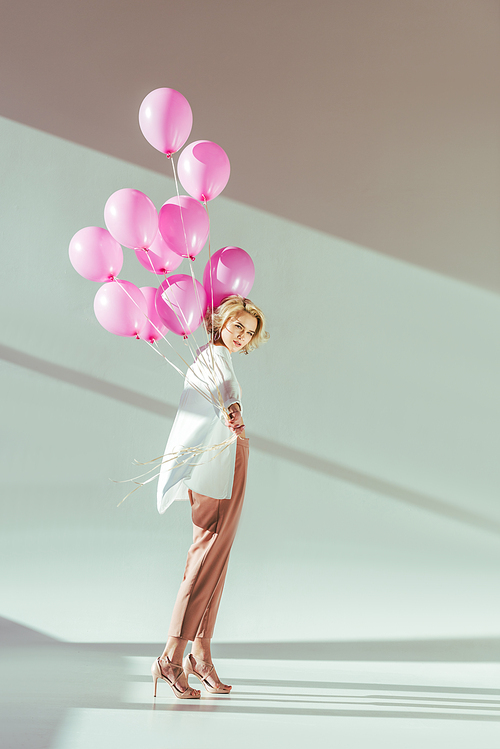 beautiful fashionable young woman holding pink balloons and  on grey