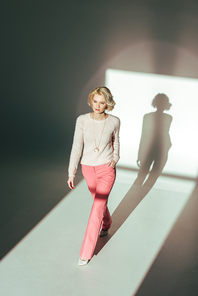 high angle view of beautiful blonde woman in trendy pink clothes walking in studio