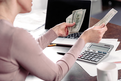 cropped shot of woman counting money at table with laptop