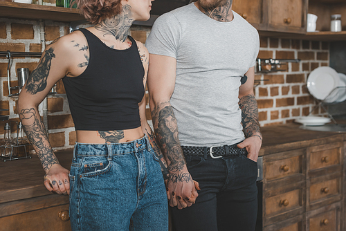 cropped view of tattooed couple holding hands in kitchen