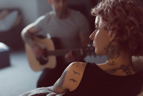 boyfriend playing on acoustic guitar for his tattooed girlfriend at home