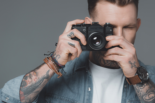 stylish young tattooed man photographing with camera isolated on grey