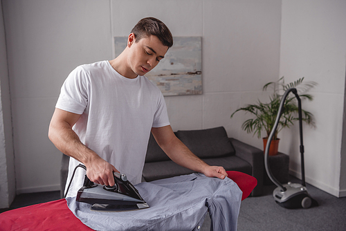 handsome man ironing shirt on ironing board in living room