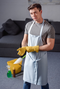 handsome man wearing rubber gloves for cleaning and looking at camera in living room