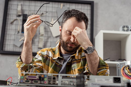 tired man holding glasses in hand with eyes closed against broken computer