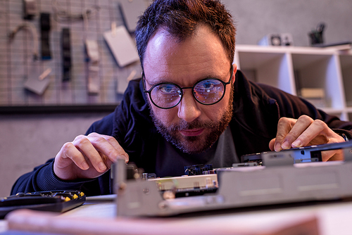 man in glasses looking on broken detail on table