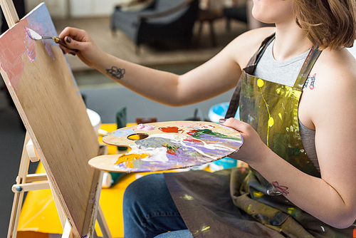 Young inspired girl applying primer on canvas in light studio