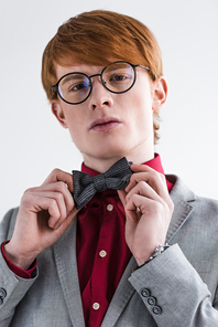 Low angle view of male fashion model in eyeglasses adjusting bow tie isolated on grey