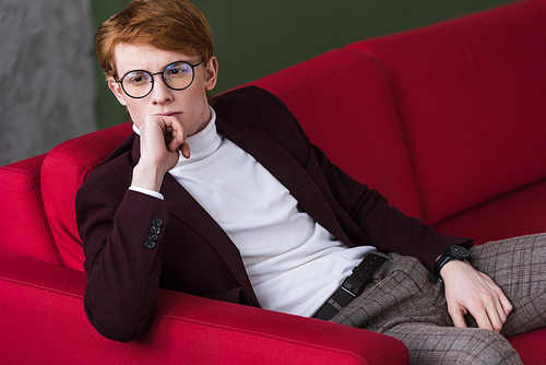 Young male fashion model in eyeglasses sitting on couch