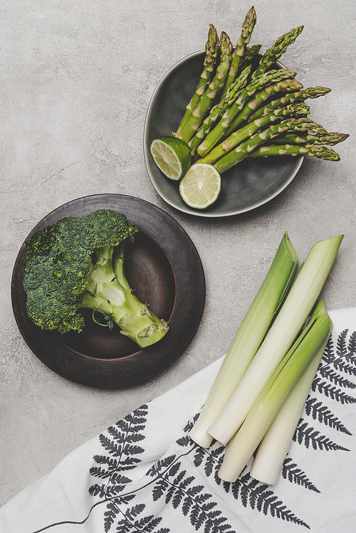 top view of fresh healthy green vegetables on plates and napkin on grey