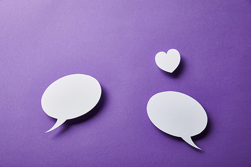 white speech bubbles and small paper heart on purple surface