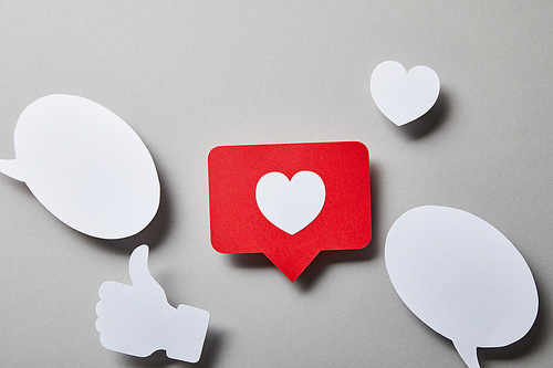 red like card, speech bubbles, thumbs up and small paper heart on white surface