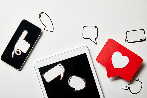 digital tablet and smartphone with paper thought and speech bubbles, paper heart, pointing card on white surface