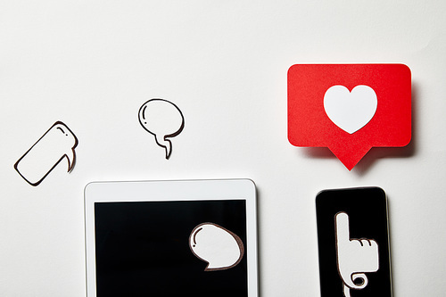 digital tablet and smartphone with paper thought and speech bubbles, paper heart, pointing card on white surface