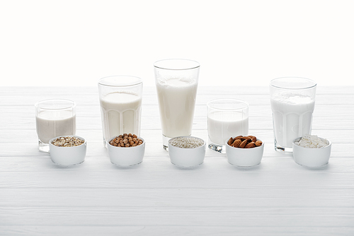 glasses with coconut, chickpea, oat, drick and almond milk with ingredients in bowls isolated on white