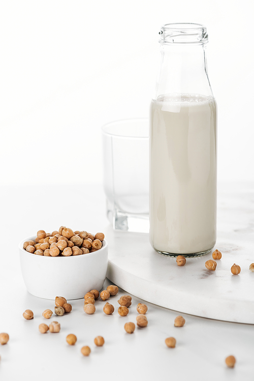 vegan chickpea milk in bottle near chickpea in bowl and empty glass isolated on white