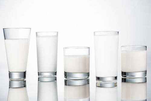row of glasses with organic fresh vegan milk on grey background with reflection