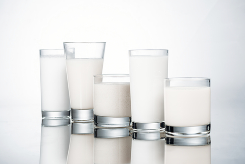 row of glasses with fresh alternative milk on grey background with reflection