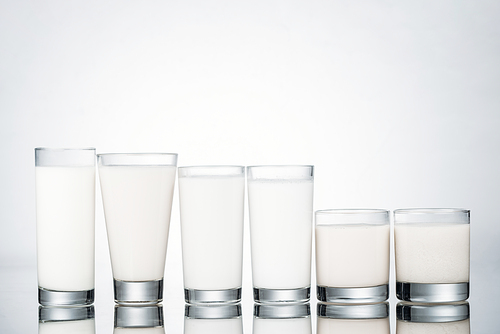 row of glasses with organic vegan milk on grey background