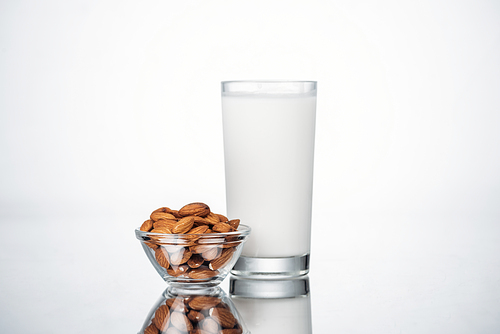 almond vegan milk in glass near bowl with nuts on grey background