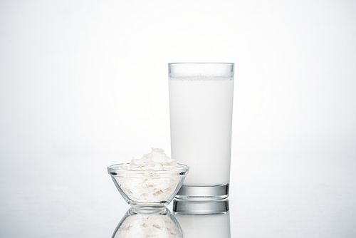 coconut vegan milk in glass near bowl with coconut slices on grey background