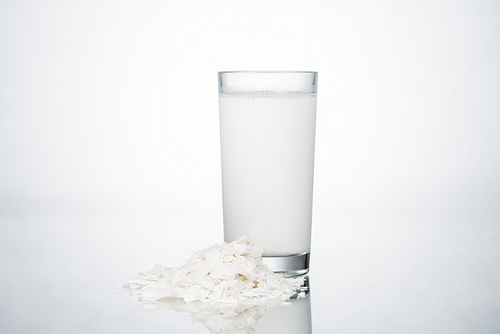 coconut vegan milk in glass near coconut slices on grey background