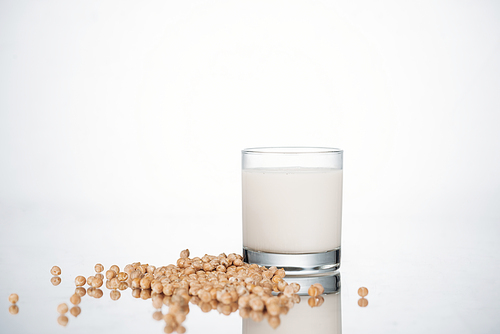 chickpea vegan milk in glass near scattered beans on grey background