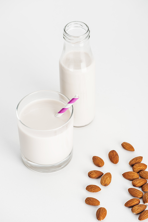 organic almond milk in bottle and glass with straw near scattered almonds