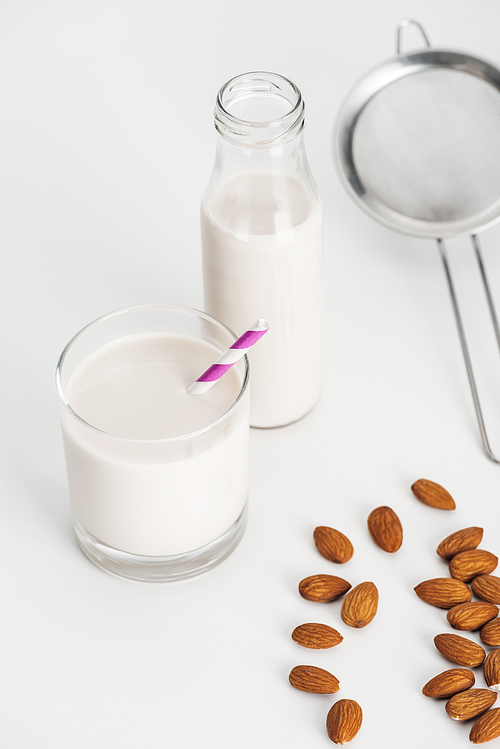 organic almond milk in bottle and glass with straw near scattered almonds and sieve