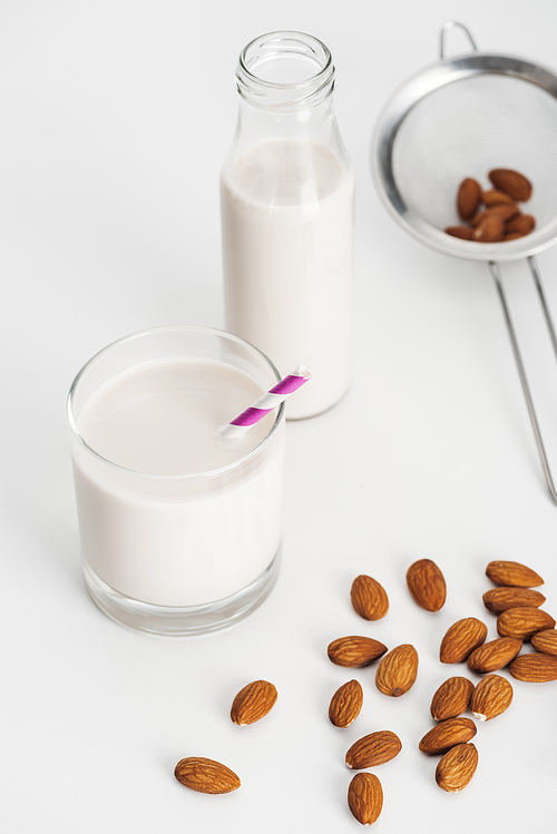 fresh almond milk in bottle and glass with straw near scattered almonds and sieve