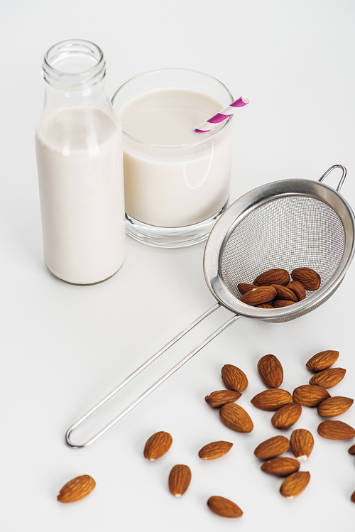 vegan almond milk in bottle and glass with straw near scattered almonds and sieve