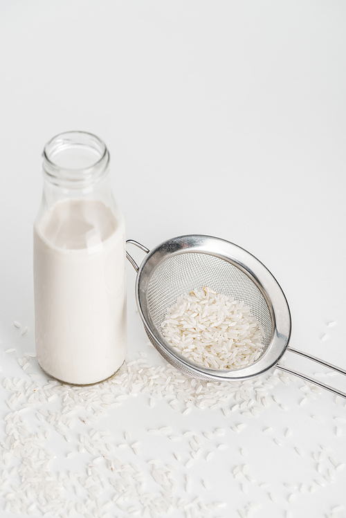 rice milk in bottle near scattered rice and sieve on grey background