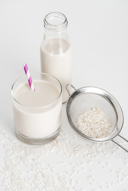 drick milk in bottle and glass with straw near scattered drick and sieve on grey background