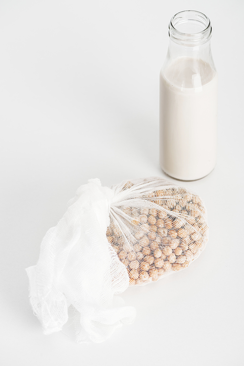 chickpea in white cheesecloth near bottle with vegan chickpea milk on grey background