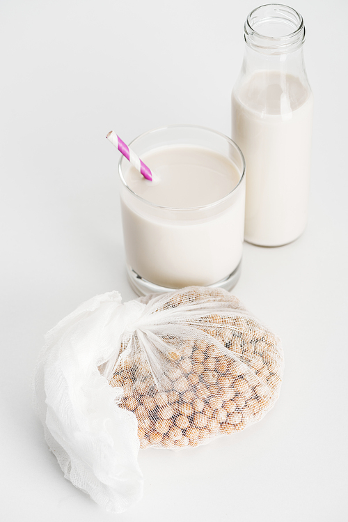 chickpea in white cheesecloth near bottle and glass with vegan chickpea milk on grey background