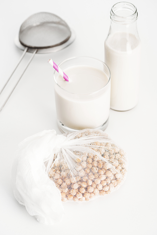 chickpea in white cheesecloth near bottle and glass with vegan chickpea milk and sieve on grey background