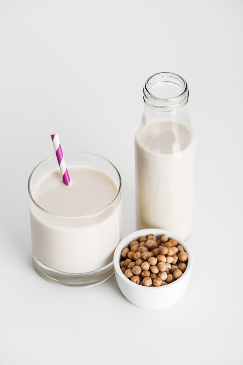 chickpea in bowl near bottle and glass with vegan chickpea milk on grey background