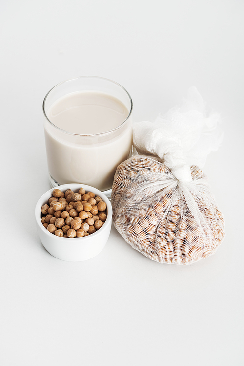 chickpea in bowl and cheesecloth near vegan chickpea milk in glass on grey background