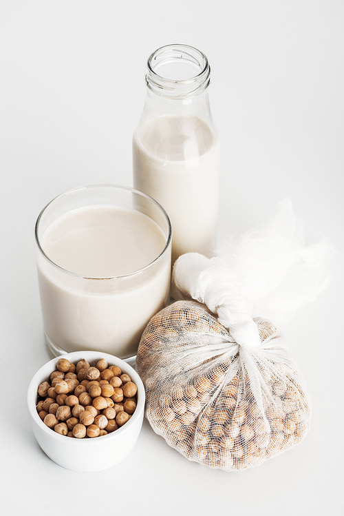 chickpea in bowl and cheesecloth near vegan chickpea milk in glass and bottle on grey background