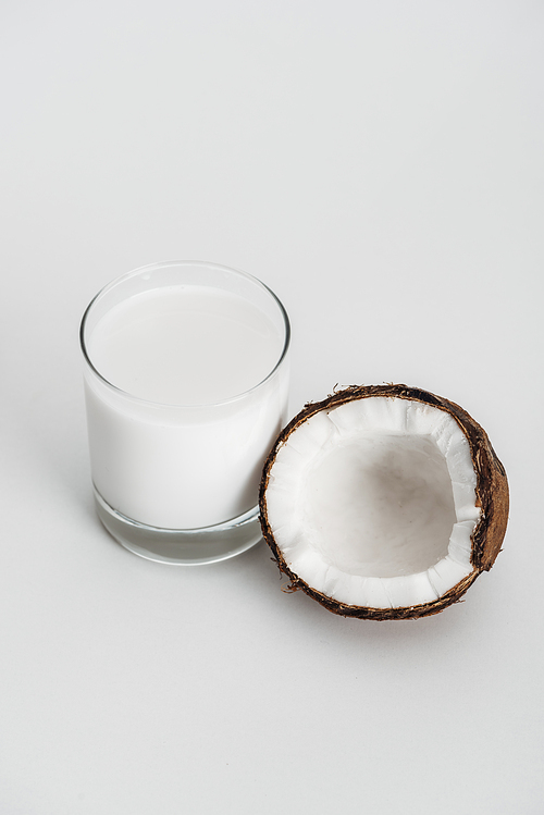 organic vegan coconut milk in glass near coconut half on grey background