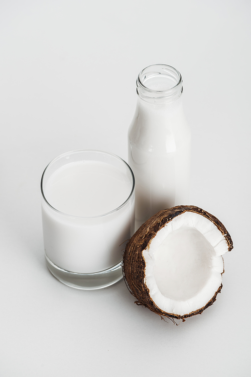 organic vegan coconut milk in glass and bottle near coconut half on grey background