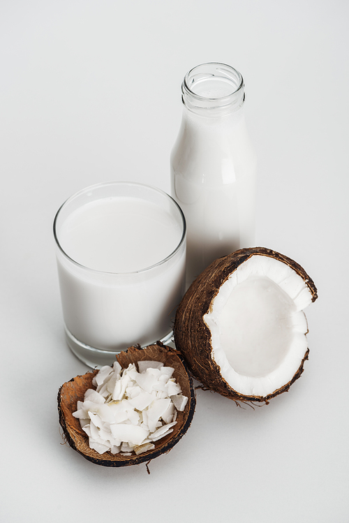 organic vegan coconut milk in glass and bottle near coconut half and coconut chips on grey background