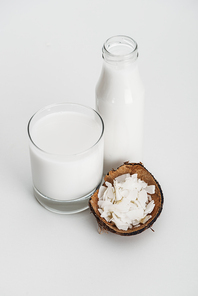 organic vegan coconut milk in glass near coconut chips on grey background